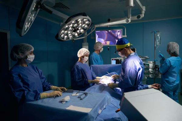 Surgeon with head camera operates on patient in a modern operating room, the patient under anesthesia lies on the table