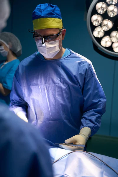 Team of doctors led by leading surgeon at workplace in operating room, the surgeon has a scalpel in his hand