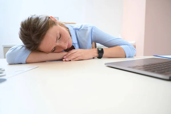 努力工作的疲倦女性的近照正在休息 同时把头放在屋里的桌子上 — 图库照片