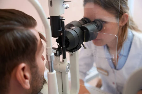 女性眼科医生侧视画像是在临床检查男性患者视力时 通过缝隙灯进行的 — 图库照片
