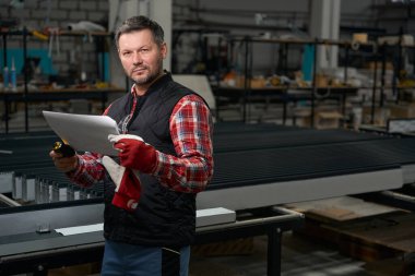 Metal yapının üretimi için atölyedeki teknik belgeleri inceleyen adam