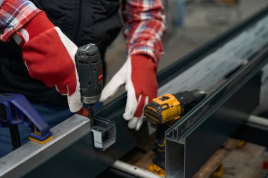 İki çelik detayı ve atölyede elektrikli tornavida kullanan adam.