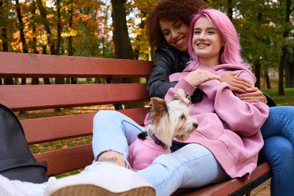 Счастливая Женщина Собакой Сидящей Скамейке Обнимаемая Своей Любящей Девушкой — стоковое фото