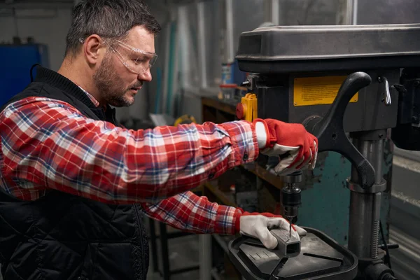 保護メガネと手袋の男性は 機器上の鋼のプロフィールに穴を作る — ストック写真