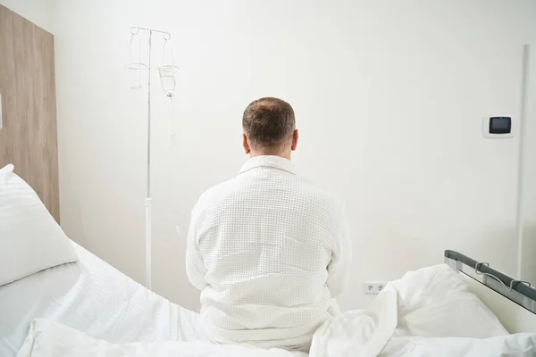 一位身份不明的男性病人坐在医院的病床上 他的后视镜出现了 — 图库照片