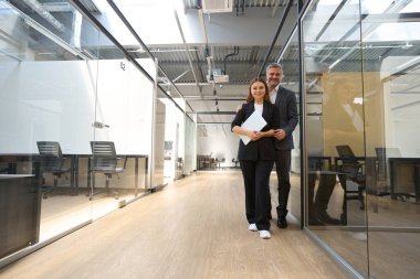 Genç, gülümseyen bir kadın ve ofis elbiseli bir adam birlikte çalışıyor, dizüstü bilgisayarı tutuyor ve kameraya bakıyor.