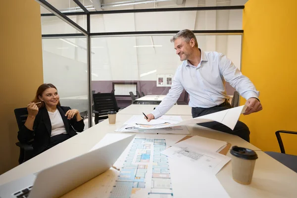 男はテーブルの近くに立って 建築計画を見て オフィスの女性と議論する — ストック写真