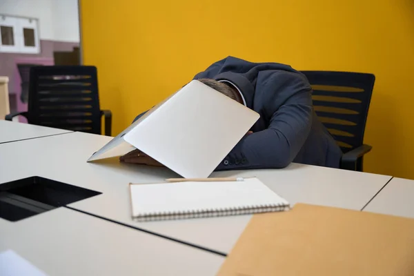 在商务中心 坐在椅子上的人在用笔记本电脑盖住自己的身体后 在桌边睡着了 — 图库照片