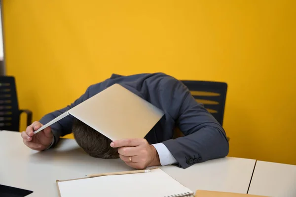 在商务中心 男人躺在办公桌前 用笔记本电脑遮住自己的工作服 — 图库照片
