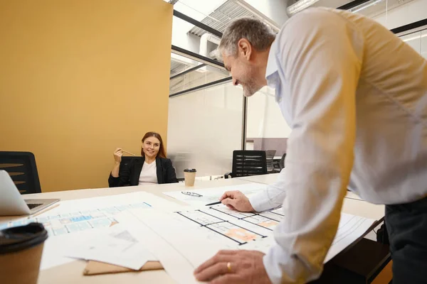 建築計画を見てオフィスの女性と話してテーブルの近くに立つ建築家 — ストック写真