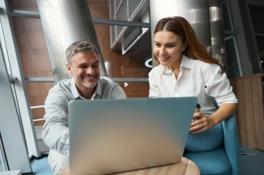 Ofiste dizüstü bilgisayarın yanında oturan mutlu kadın, yanında oturan ve konuşan ekran adamına bakıyor