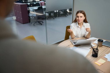 Dizüstü bilgisayarın yanındaki masada oturan genç bayan birlikte çalışıyor ve çalışanlarla konuşuyor.