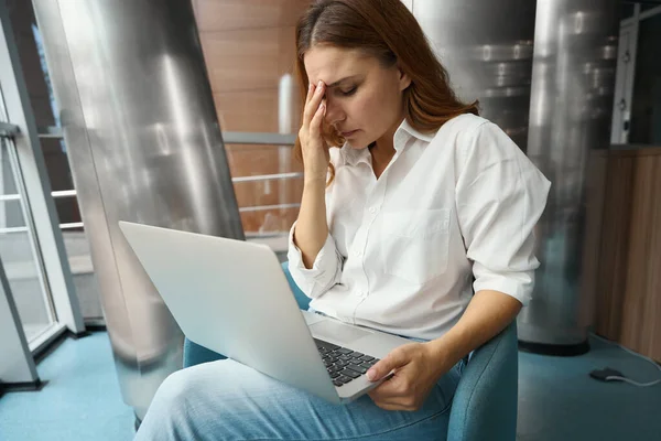 Triste Jovem Mulher Sentada Escritório Segurando Laptop Tocando Cabeça Com — Fotografia de Stock