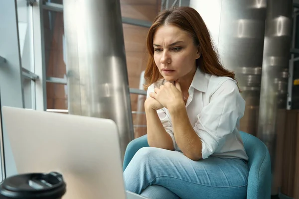 悲しい若い女性がオフィスに座ってノートパソコンの画面を見て待ってる — ストック写真