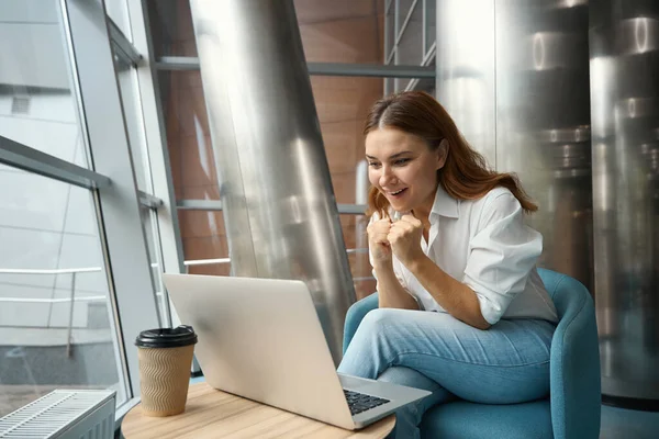 幸せな若い女性がオフィスに座ってノートパソコンの画面を見て喜び — ストック写真