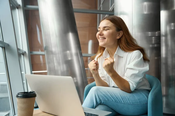 快乐的年轻女性坐在笔记本电脑旁的办公室里 抬起头来 兴高采烈 — 图库照片