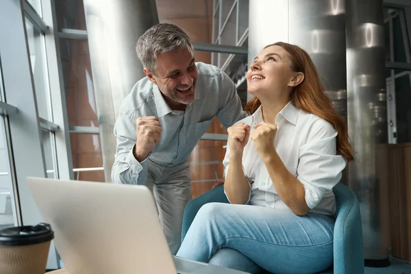 幸せな若い女性はノートパソコンの近くのオフィスに座って見て喜び男は近くに立って — ストック写真