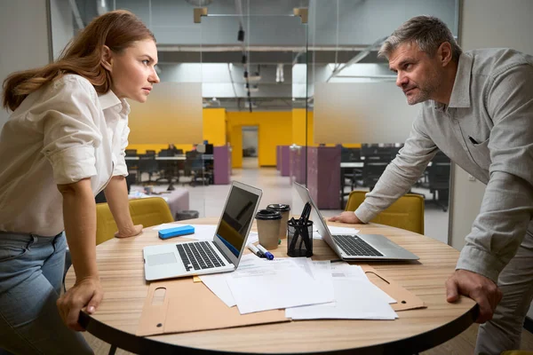 ノートパソコンでテーブルの近くに立っているオフィスの服を着た若い女性と男が — ストック写真
