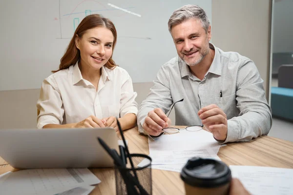 女性はノートパソコンの近くのテーブルに座って オフィスの服を着た笑顔の男と画面を見て — ストック写真