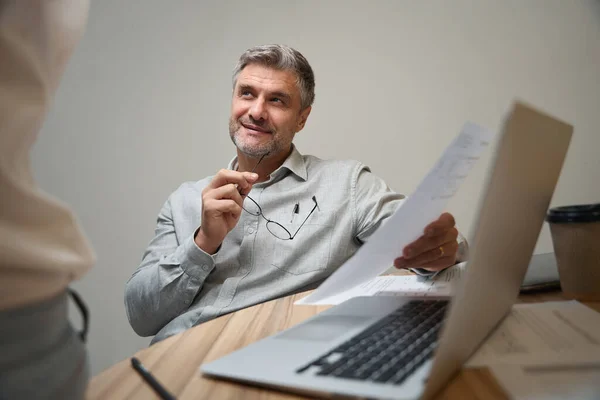 Hombre Sonriente Sentado Junto Mesa Cerca Computadora Portátil Coworking Sosteniendo —  Fotos de Stock