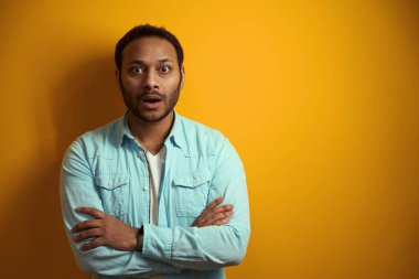 Mavi gömlekli sürpriz adam ofiste duruyor, sarı arka plan üzerinde çalışmaya hazır.