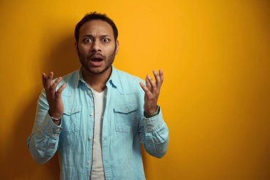 Şaşkın mavi gömlekli erkek ofiste duruyor, sarı arka planda çalışmaya hazır.