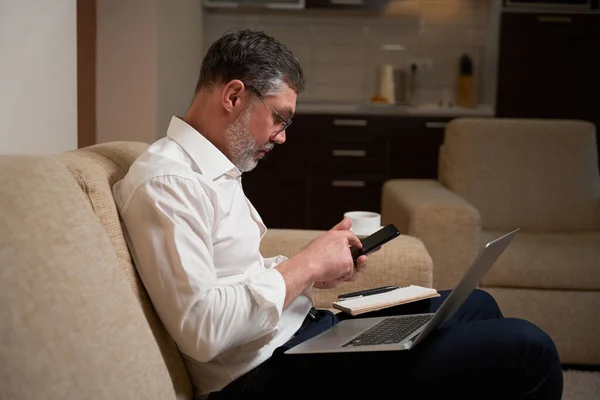 身穿商务服装的男性坐在沙发上 拿着笔记本电脑 与客户通电话 — 图库照片