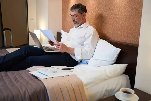 身穿商务服装的成年人坐在床上 拿着笔记本电脑和电话 — 图库照片