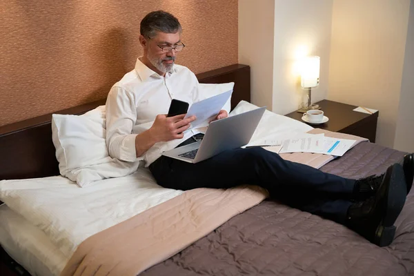 Kıyafetleri Içinde Profesyonel Bir Erkek Elinde Dizüstü Bilgisayarla Yatakta Oturuyor — Stok fotoğraf