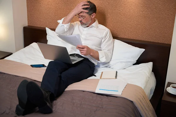 穿着工作服的工人坐在床上 拿着笔记本电脑 阅读文件 — 图库照片