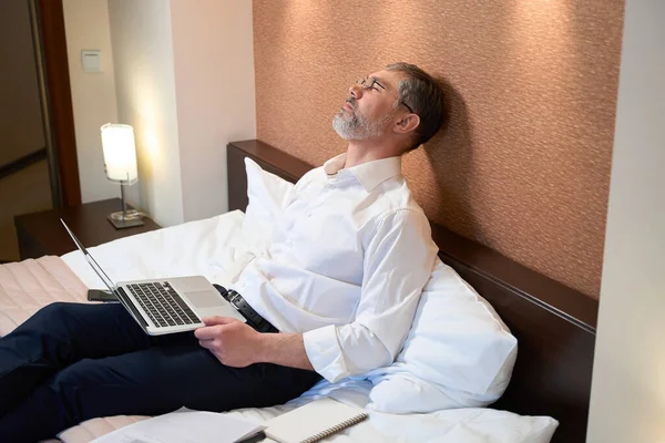 穿着工作服的专业人员坐在床上 拿着笔记本电脑睡觉 — 图库照片