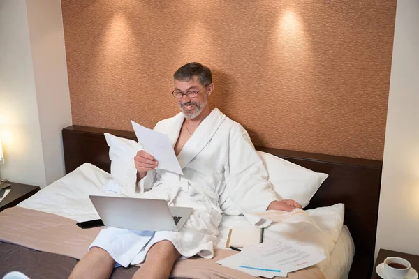 Masculino Roupão Sentado Cama Segurando Laptop Lendo Documentos Hotel — Fotografia de Stock