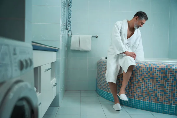 Adult Male White Bathrobe Bathroom Sitting Edge Bath Checking Water — Stock Photo, Image