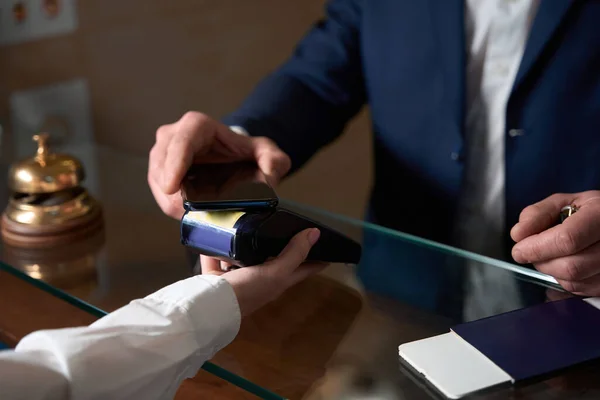 レセプションエリアの近くに立っているビジネス服の女性 カード決済機を保持 携帯電話で支払う男 — ストック写真