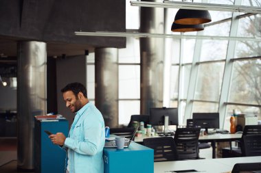 Masada dizüstü bilgisayarla duran ve iş merkezinde telefon kullanan mutlu bir erkek.