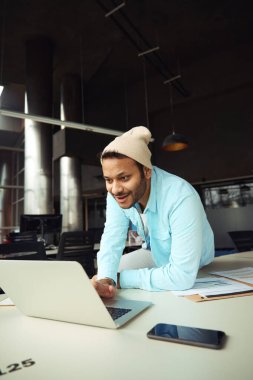Başlıklı mutlu bir erkek masada oturuyor ve ofiste dizüstü bilgisayarda yazıyor.