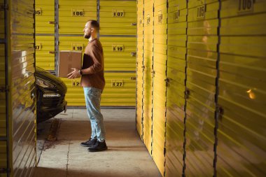 Depoda karton kutuyu tutan genç adamın yan görüş fotoğrafı.