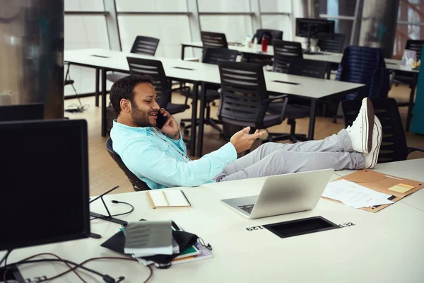 若い男性は椅子に座って 仕事でスマートフォンでクライアントと会話をしています — ストック写真