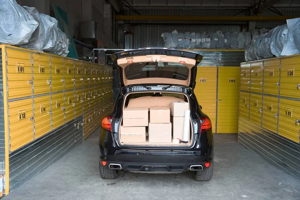 箱を積んだ開いたトランクを持つ倉庫に立つ大型車 — ストック写真