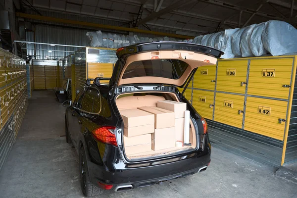 貨物でいっぱいのオープントランクを持つ倉庫に立つ黒い車 — ストック写真