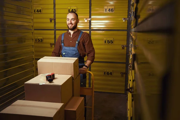 箱を持ったローダーを持ちながら倉庫に立つ男の笑顔 — ストック写真