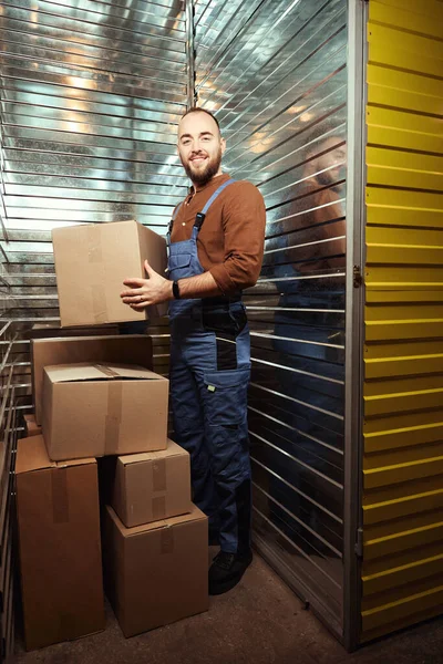 段ボール箱を持ちながら収納室に立つ大人の笑顔の男性の完全な長さの写真 — ストック写真