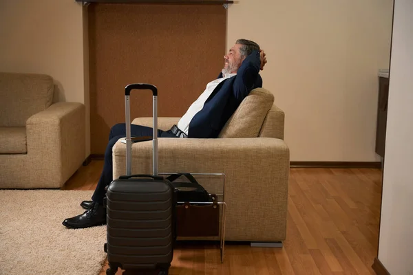 穿着西装坐在手提箱旁边的快乐男士们正在宾馆休息 — 图库照片