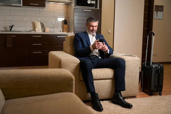 Homem Sorridente Terno Negócios Sentado Cadeira Usando Smartphone Hotel — Fotografia de Stock