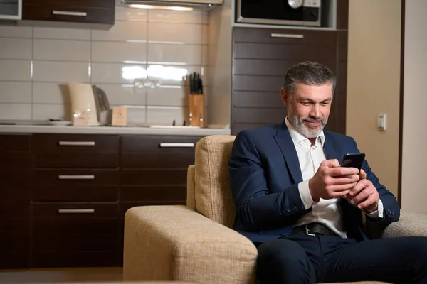 大人の男ビジネススーツの椅子に座って ホステルの部屋で電話を使用して — ストック写真