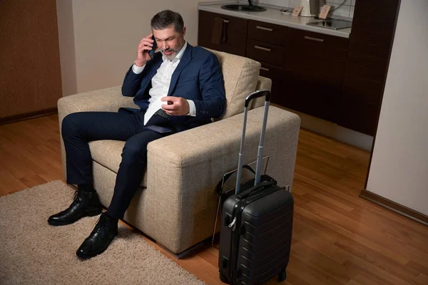 Mężczyzna Siedzi Fotelu Dzwoni Przez Telefon Wizytówki Hotelu — Zdjęcie stockowe