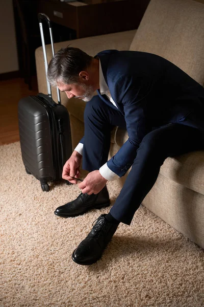 在宾馆里 一个成年人坐在沙发上 紧挨着手提箱 系着鞋带 — 图库照片