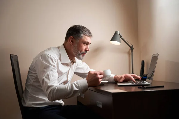 Masada Elinde Fincanla Oturan Dizüstü Bilgisayara Bakan Bir Erkek — Stok fotoğraf