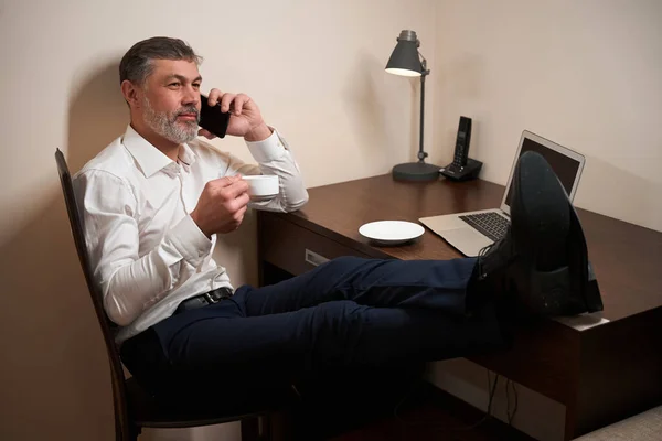 Yetişkin Bir Adam Elinde Fincanla Sandalyede Oturuyor Otelde Telefonla Konuşuyor — Stok fotoğraf
