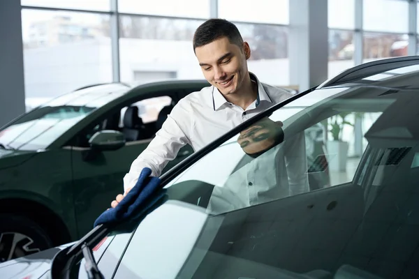 穿着办公室衣服的快乐男人擦拭着一辆闪闪发亮的新车的车身 在一家汽车经销店里看车窗 — 图库照片